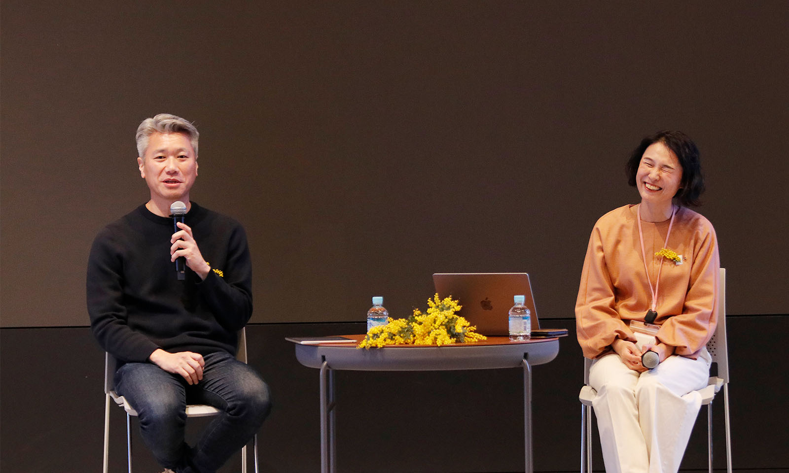 ステージ前方に座りマイクを持ちながら話す越川さんと、その話を聞きながら参加者に笑顔を向ける西村さん